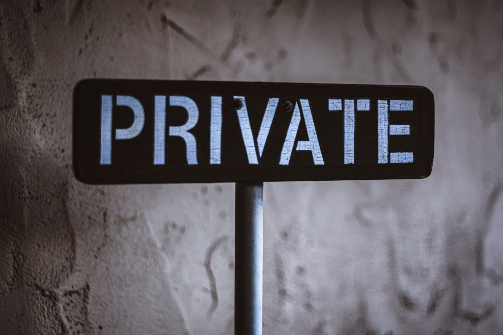 Black sign on metal pole with the word PRIVATE against a grey textured wall
